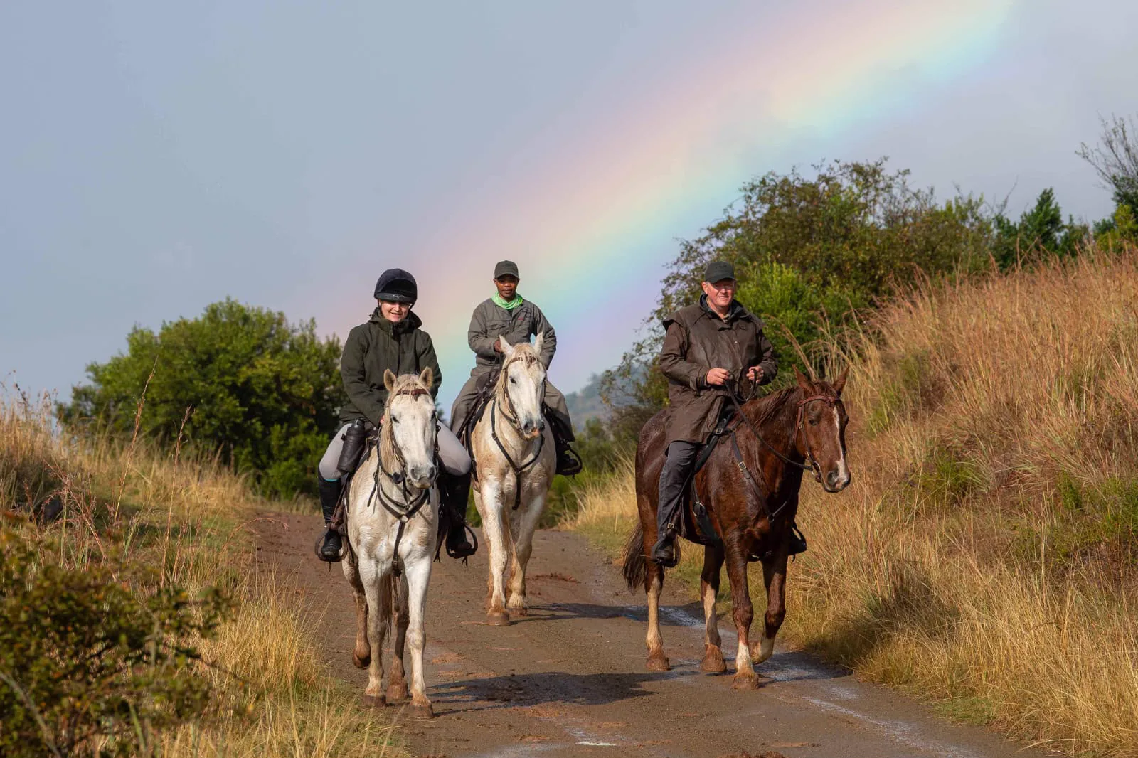 Mounted riders beneath a rainbow in open Eastern Cape country